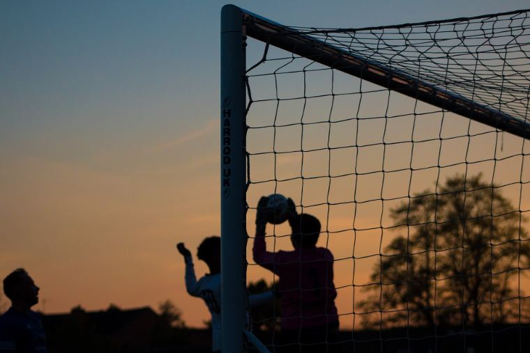 A goalkeeper silhouetted against a sunset, catching the ball